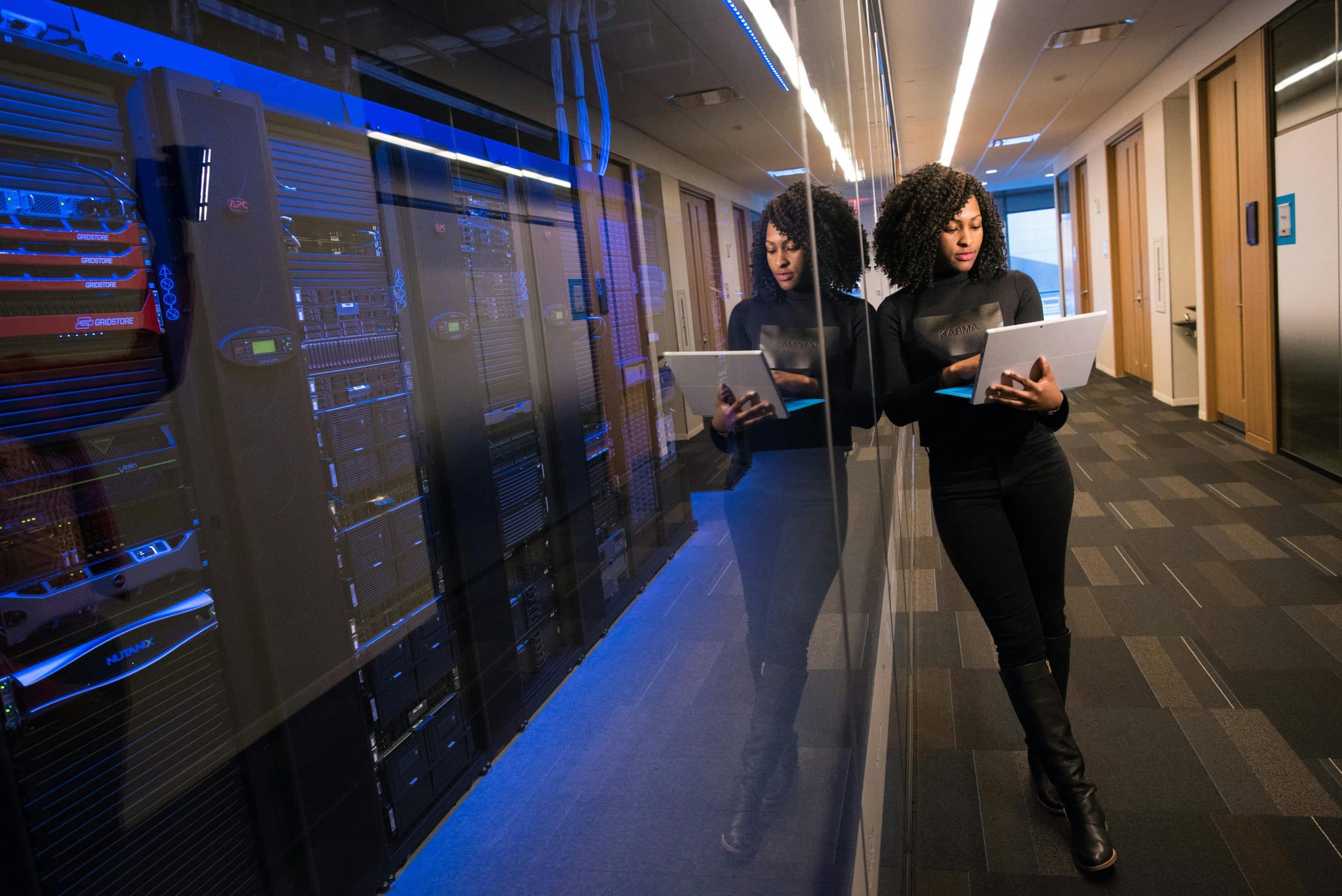 Engineer with a laptop standing in a data centre corridor surrounded by server racks, representing the cloud infrastructure and technical backbone supporting enterprise data mesh operations.